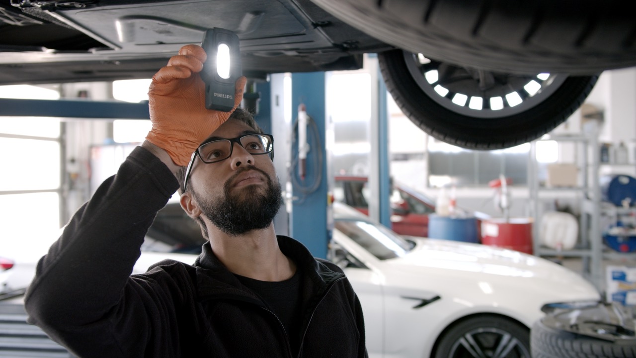 Ein Mechaniker des CarCenter Erding prüft einen BMW auf der Hebebühne von unten mit der Lampe